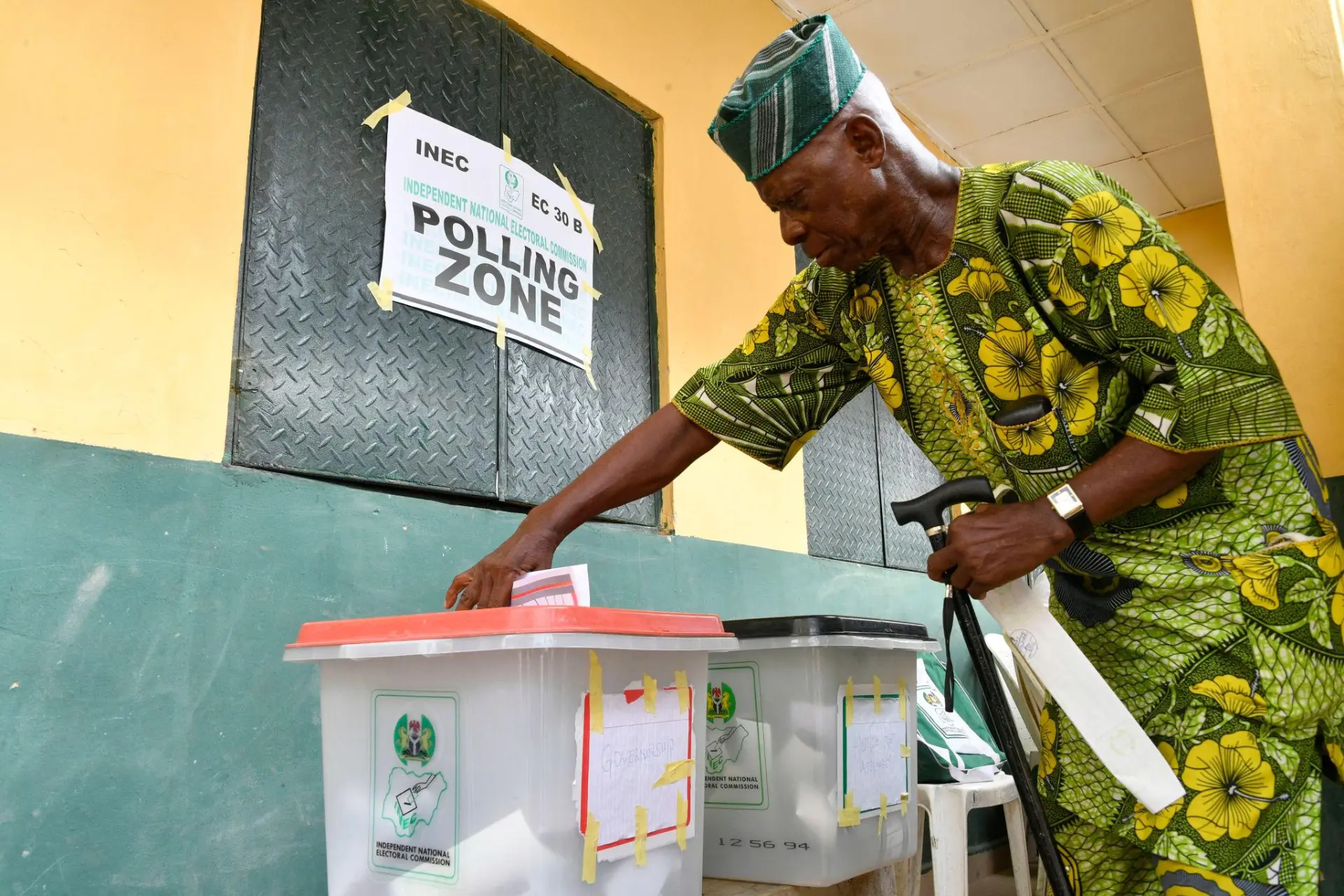 An elderly voter casting his ballot beside an INEC polling zone sign